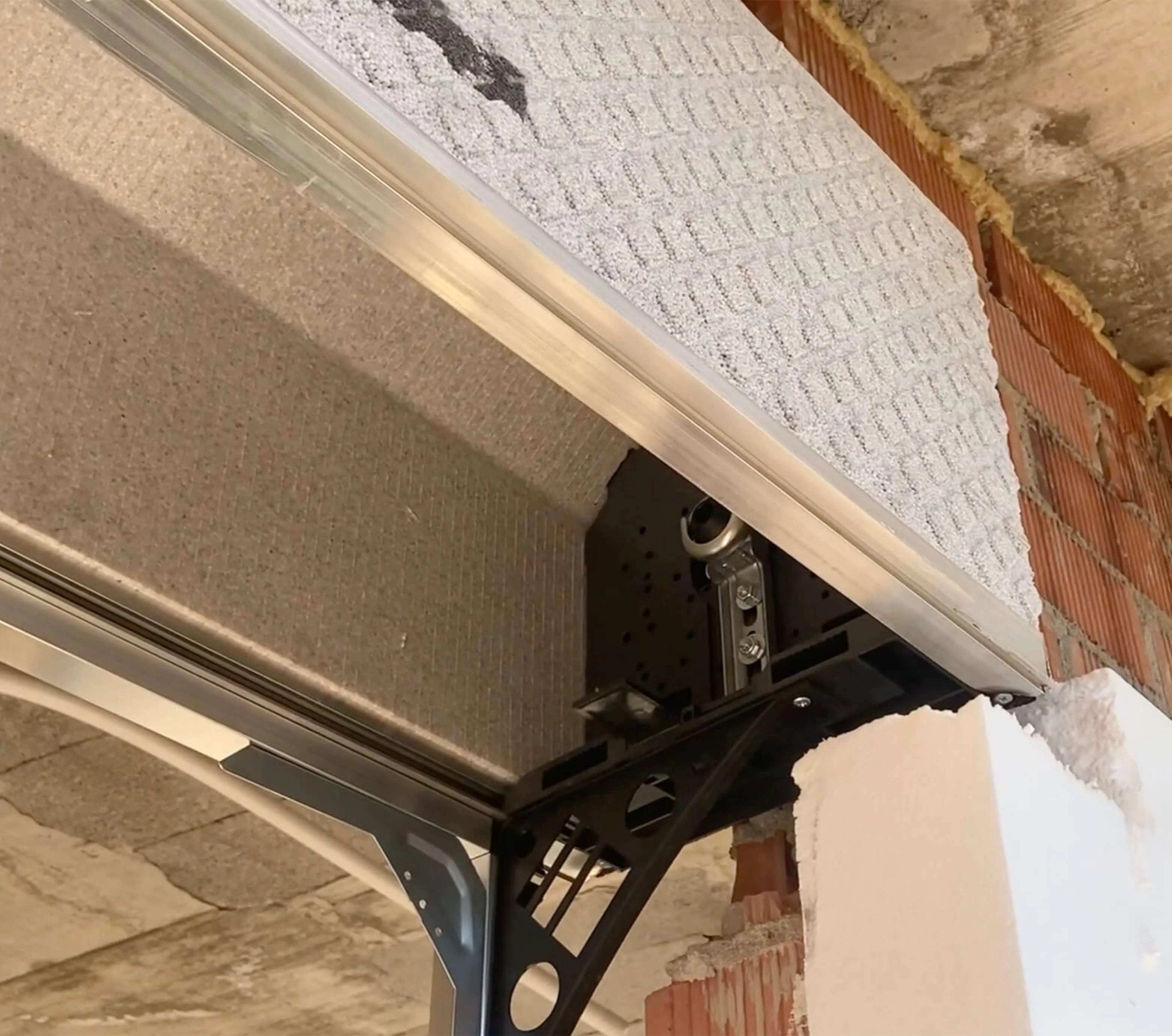 Detalle inferior del cajón COMPACTBOX con la jaula de acero zincado y el perfil de aluminio sobre pared de ladrillo