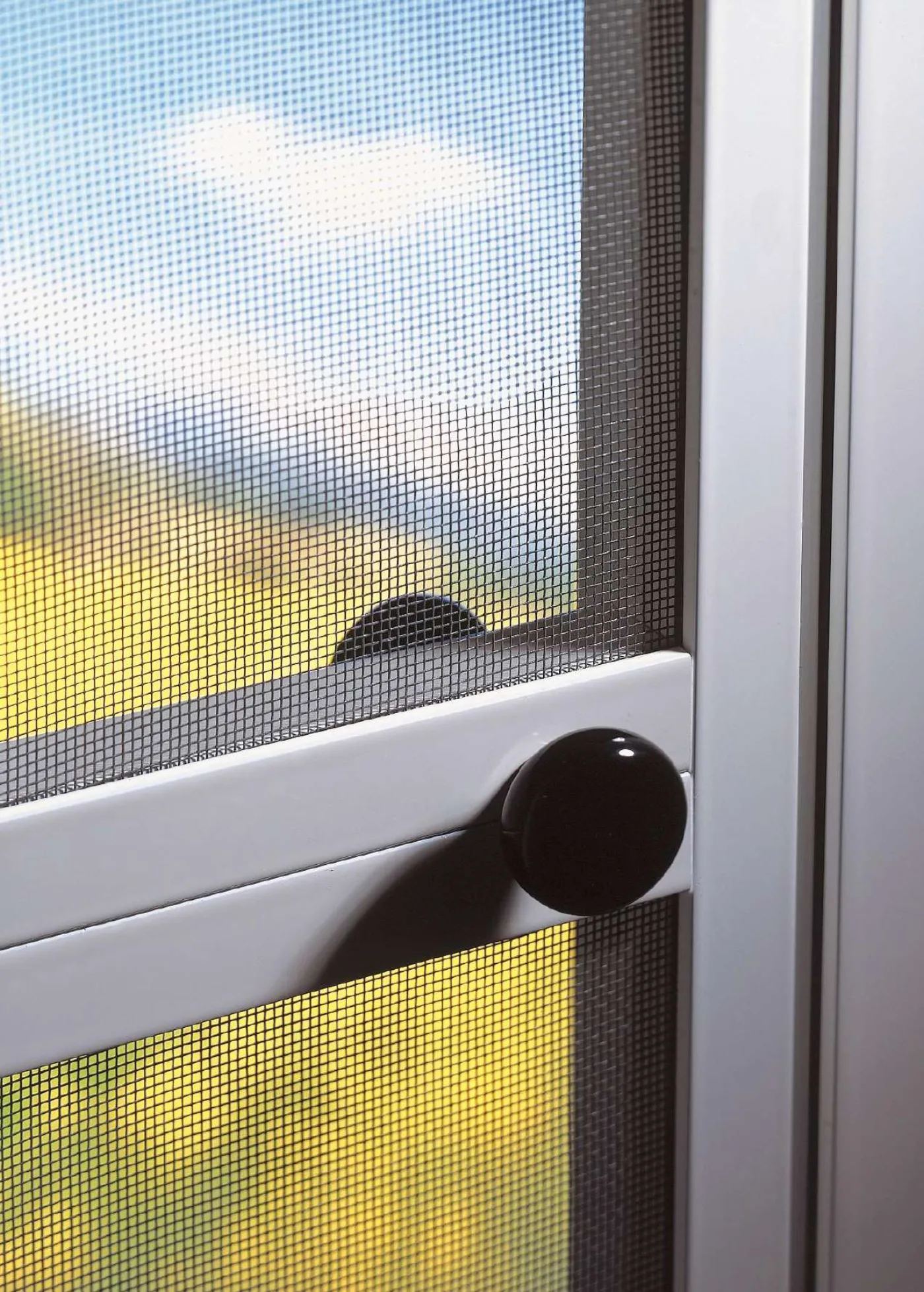 Detalle de mosquitera de puerta abatible con manilla negra y paisaje al fondo a través de la tela