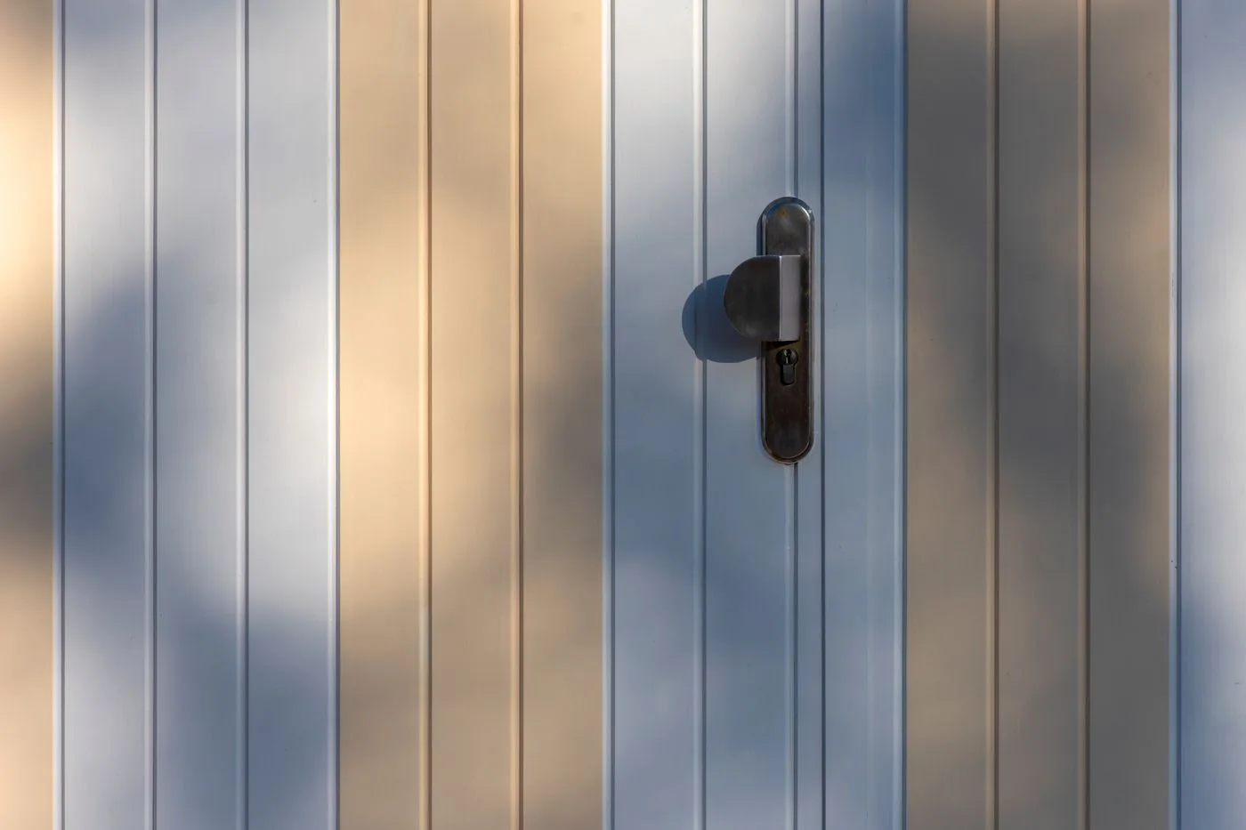 Detalle del tirador y cerradura de una puerta de aluminio de lamas verticales con luz natural