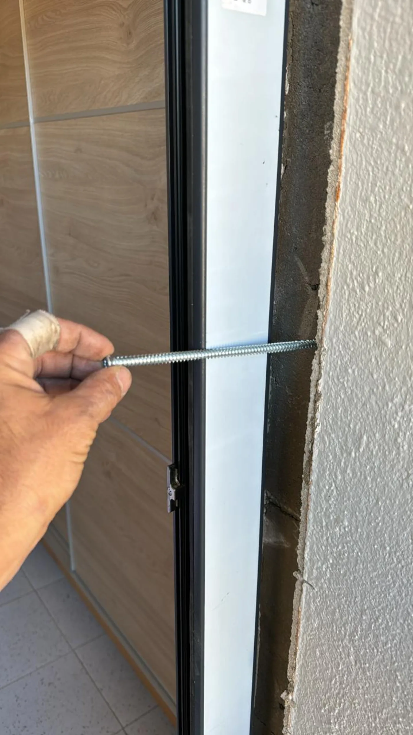 Cargol llarg d'alta resistència travessant el marc de PVC fins al mur estructural durant la fixació