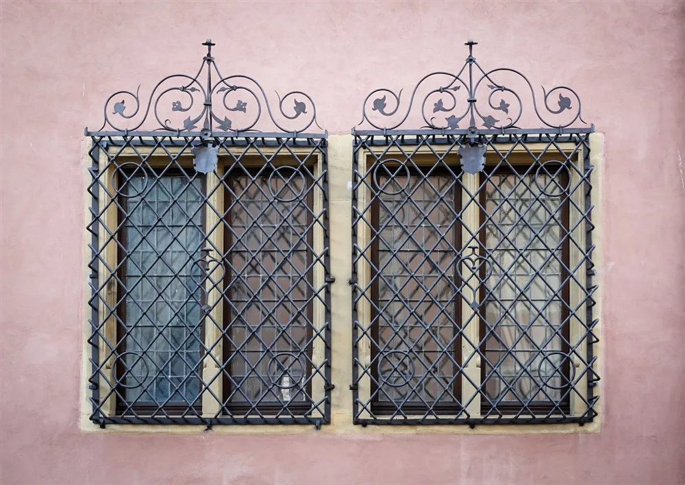 Reixa de seguretat de gelosia de ferro amb remat ornamental en una façana